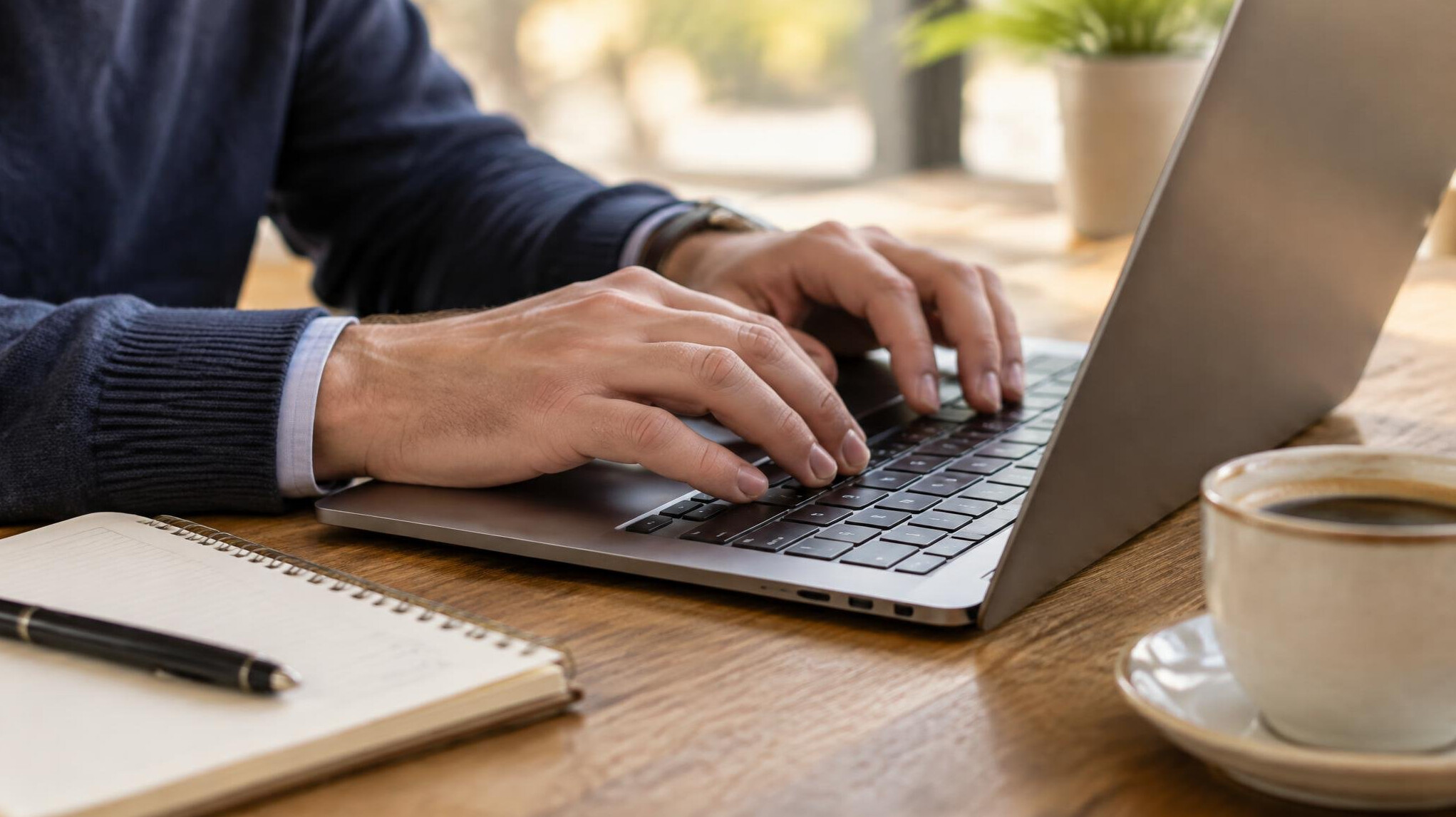 Hands typing on a laptop at a table with coffee